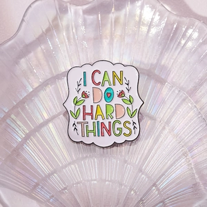 Macro shot of square enamel pin with I CAN DO HARD THINGS text and floral details