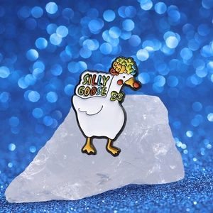 Détail d'un pin's émaillé représentant une oie blanche avec nœud vert et texte coloré