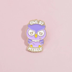 Close-up of purple enamel owl pin with Owl By Myself text and gold metal edges