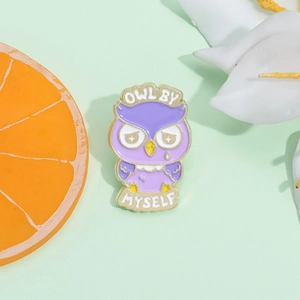 Close-up of purple enamel owl brooch with Owl By Myself text on a green background