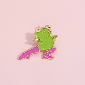 Detail of funny green frog enamel pin wearing glittery pink boots on pink background