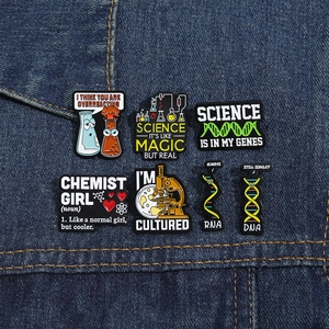 Detailed close-up of six creative science enamel pins on blue denim fabric background