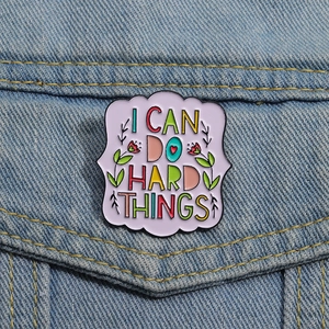 Detail of I Can Do Hard Things enamel pin on denim jacket with floral metal patterns