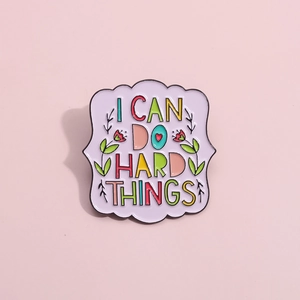 Colorful enamel floral brooch with 'I CAN DO HARD THINGS' text on a pink background