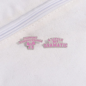 Détail de pins en émail rose avec les slogans I Support Womens Wrongs et A Little Bit Dramatic