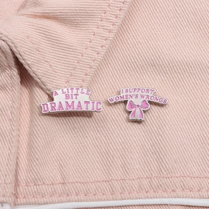 Détail de pins en émail rose avec texte féministe sur fond de tissu denim rose