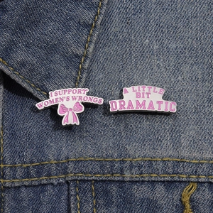 Détail de broches en émail rose sur denim avec slogans féministes et thèmes dramatiques
