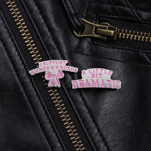 Détail de broches en émail rose avec citations sur texture de veste en cuir noir
