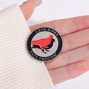 Detailed close-up of Love Birbs Hate Fascism enamel pin held against a white sweater