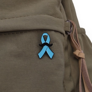 Détail d'un ruban bleu et d'un pin's moustache noire sur un sac à dos en toile vert olive