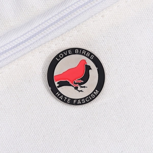 Detail of round enamel pin showing red and black birds with Love Birds Hate Fascism text