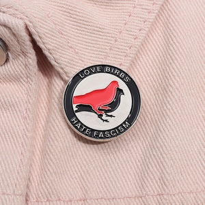 Detail of Love Birbs Hate Fascism enamel pin on pink denim fabric background