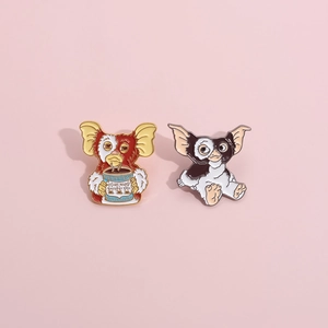 Detailed view of two cute Gremlins enamel pins on a pink background with metallic edges