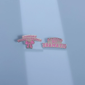 Détail de broches en émail rose avec texte A Little Bit Dramatic et finition nœud en métal