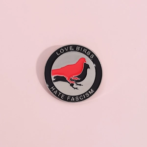 Detail of round enamel pin featuring red and black bird silhouettes and anti-fascist slogans