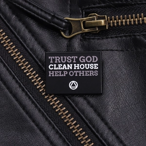 Gros plan d'un pin's émaillé noir Trust God attaché au zip d'une veste en cuir
