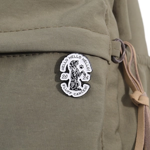 Detail of cute dog enamel pin with HELLO FLUFF CANCER text on olive canvas bag