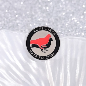 Macro shot of circular enamel pin featuring Love Birbs and Hate Fascism text on red black birds
