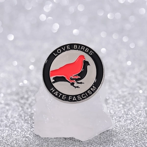 Close-up of enamel pin with bird silhouettes and Hate Fascism text on stone stand