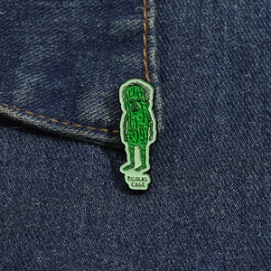 Funny green Picolas Cage enamel pin on denim jacket showing quirky cucumber design