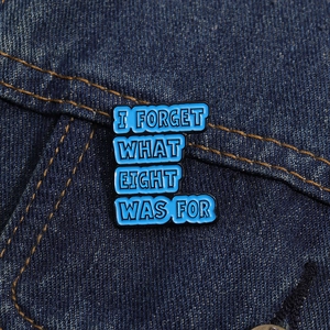 Blue enamel pin with 'I FORGET WHAT EIGHT WAS FOR' text on dark denim fabric background
