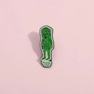 Funny cucumber enamel pin featuring Picolas Cage meme on a soft pink background