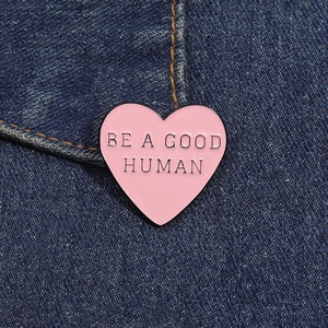 Dettaglio della spilla smaltata a cuore rosa con scritta Be A Good Human su giacca di denim