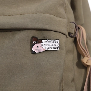 Detailaufnahme einer Cartoon-Opossum-Cowboy-Emaille-Nadel an einem grünen Rucksackgurt