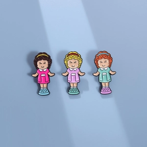 Set of three cute cartoon girl enamel pins in pink, purple, and green dresses on blue background