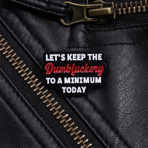 Détail du badge émaillé avec texte Let's Keep The Dumbfuckery To A Minimum sur cuir noir