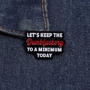 Détail d'une épinglette en émail noir avec texte humoristique sur denim bleu