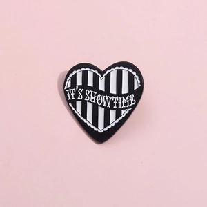 Heart-shaped black and white striped enamel pin with It's Showtime text and lace edge