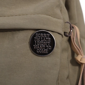 Détail macro du pin's émaillé avec texte humoristique sur tissu vert texturé