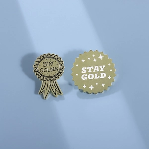 Minimalist gold medal brooch set with Stay Golden engraving on a light blue background