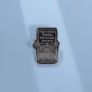 Close-up of vintage typewriter enamel brooch featuring Edgar Allan Poe quote on blue backdrop
