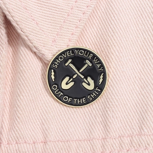 Macro shot of a round black enamel shovel brooch with gold trim on pink denim