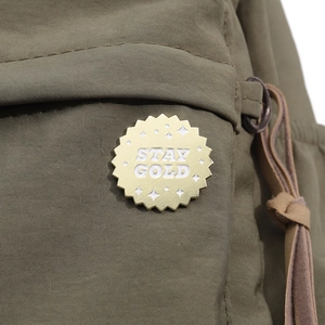 Detailed close-up of olive green canvas with Stay Gold patch and bronze hardware