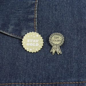 Detail of two vintage enamel STAY GOLD pins on blue denim jacket fabric