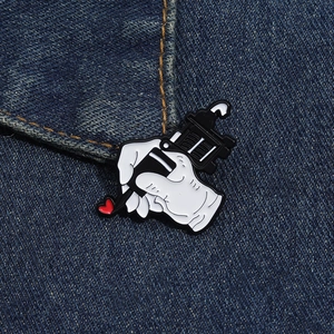 Detail van de cartoon tatoeagemachine emaille speld met een hartje op denim stof