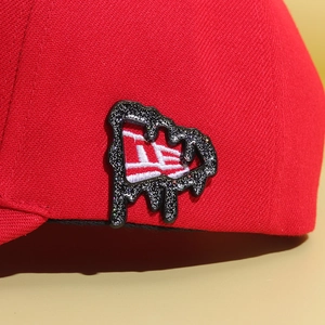Macro detail of the embroidered logo on a red textured fabric hat with glitter finish