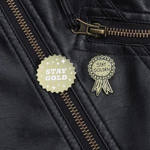 Vue macro de broches émaillées dorées Stay Gold fixées sur une veste en cuir noir de qualité