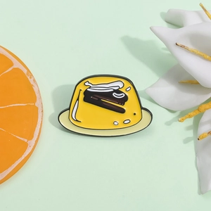 Cute yellow pudding enamel pin featuring a stapler design on light green background