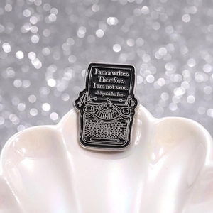 Close-up of retro typewriter enamel pin with writer quote on shiny shell background