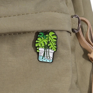 Detailed macro shot of an enamel monstera leaf pin in a beaker on green canvas background