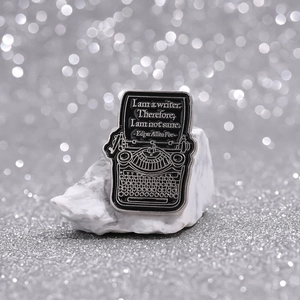 Minimalist black typewriter enamel pin featuring Edgar Allan Poe quote on marble base