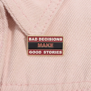 Detail of metal enamel pin badge with Bad Decisions Make Good Stories text on pink denim