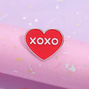 Broche en émail cœur rouge avec lettrage XOXO blanc sur un support décoratif