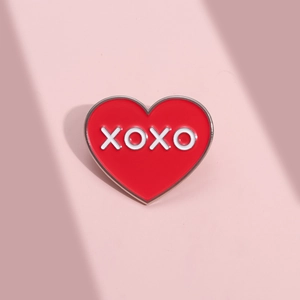 Détail d'un pin's émaillé cœur rouge avec lettres XOXO sur fond rose pastel