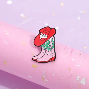 Pink western cowboy boot and red hat enamel pin with green flame patterns on display stand