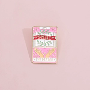 Détail du pin's émaillé rose carte de tarot avec texte The Reader et motifs de livre